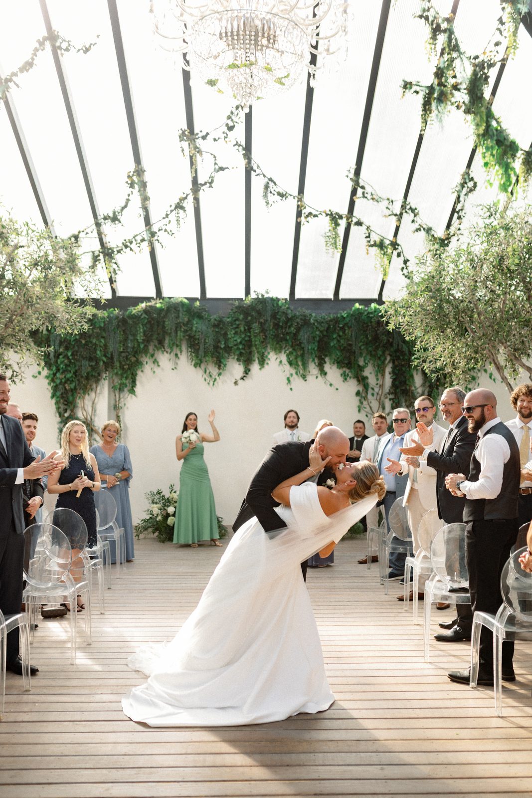 Wide ceremony frame at Greenhouse Two Rivers, natural light through the glass pavilion
